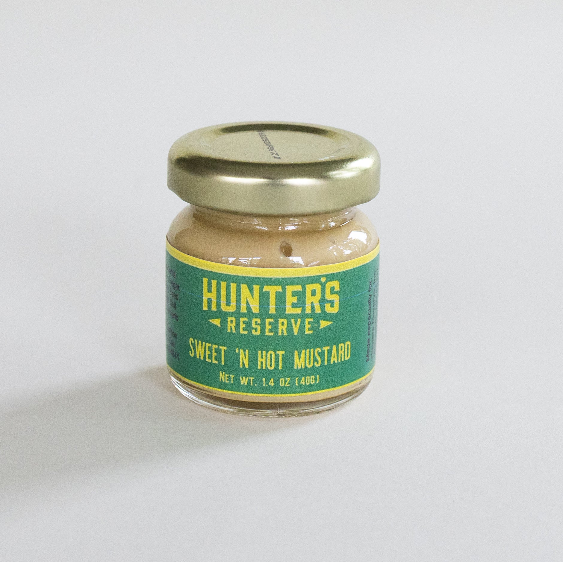 A small glass jar of Hunter's Reserve Sweet 'N Hot Mustard with a gold metal lid and a green and yellow label, set against a plain light gray background.
