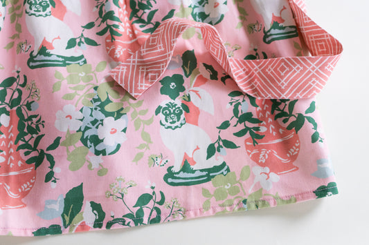 A close-up of a pink fabric garment or textile with a printed pattern of white pugs, green leaves, and coral floral motifs, folded to show the pattern and a matching pink patterned inner lining.
