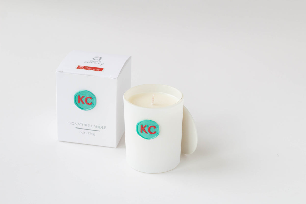 A white ceramic candle jar with a teal circular KC logo wax seal, shown next to its white packaging box on a clean white background.