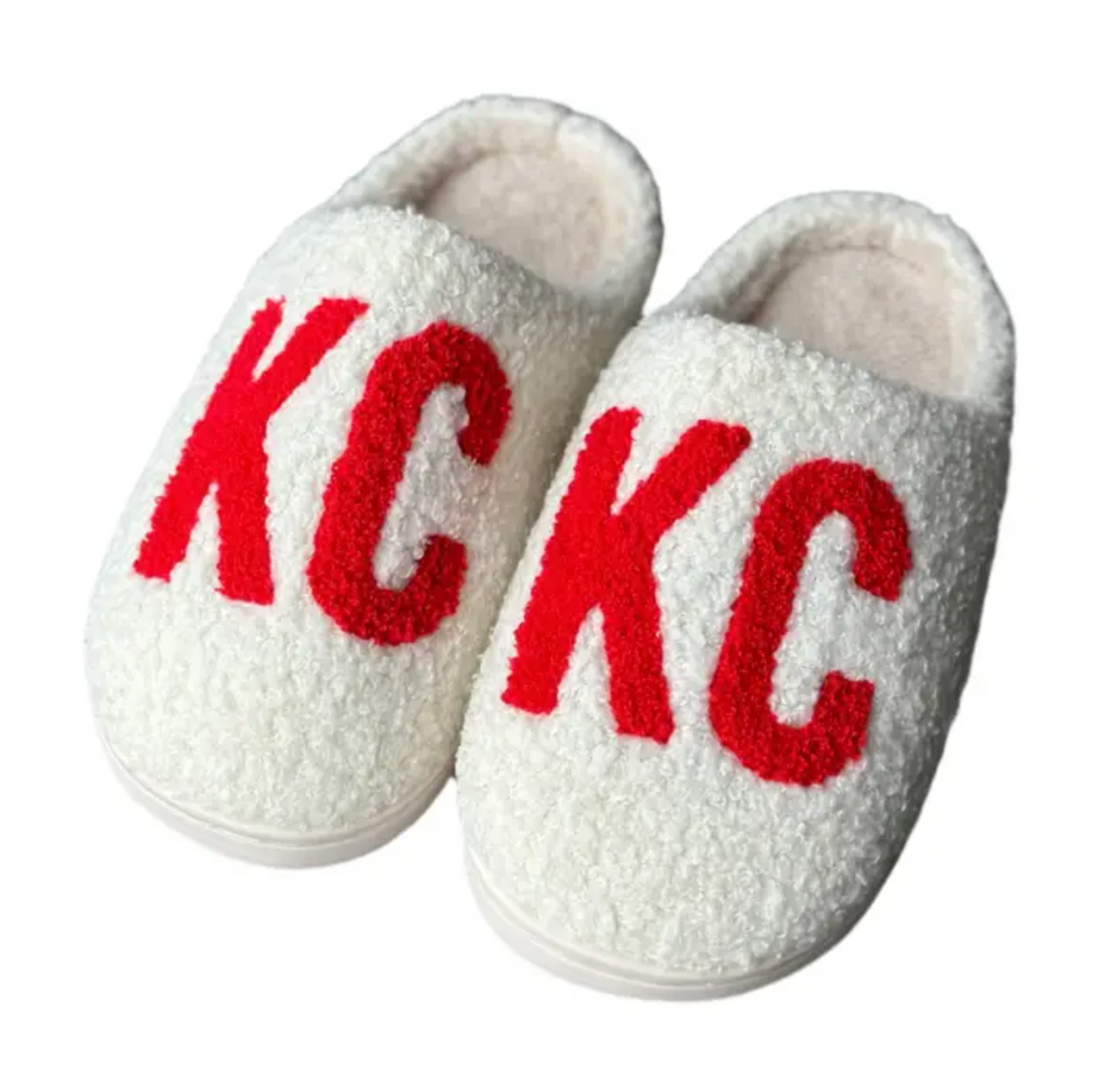 A pair of white sherpa slip-on slippers with bold red 'KC' lettering on the front, displayed against a plain white background.