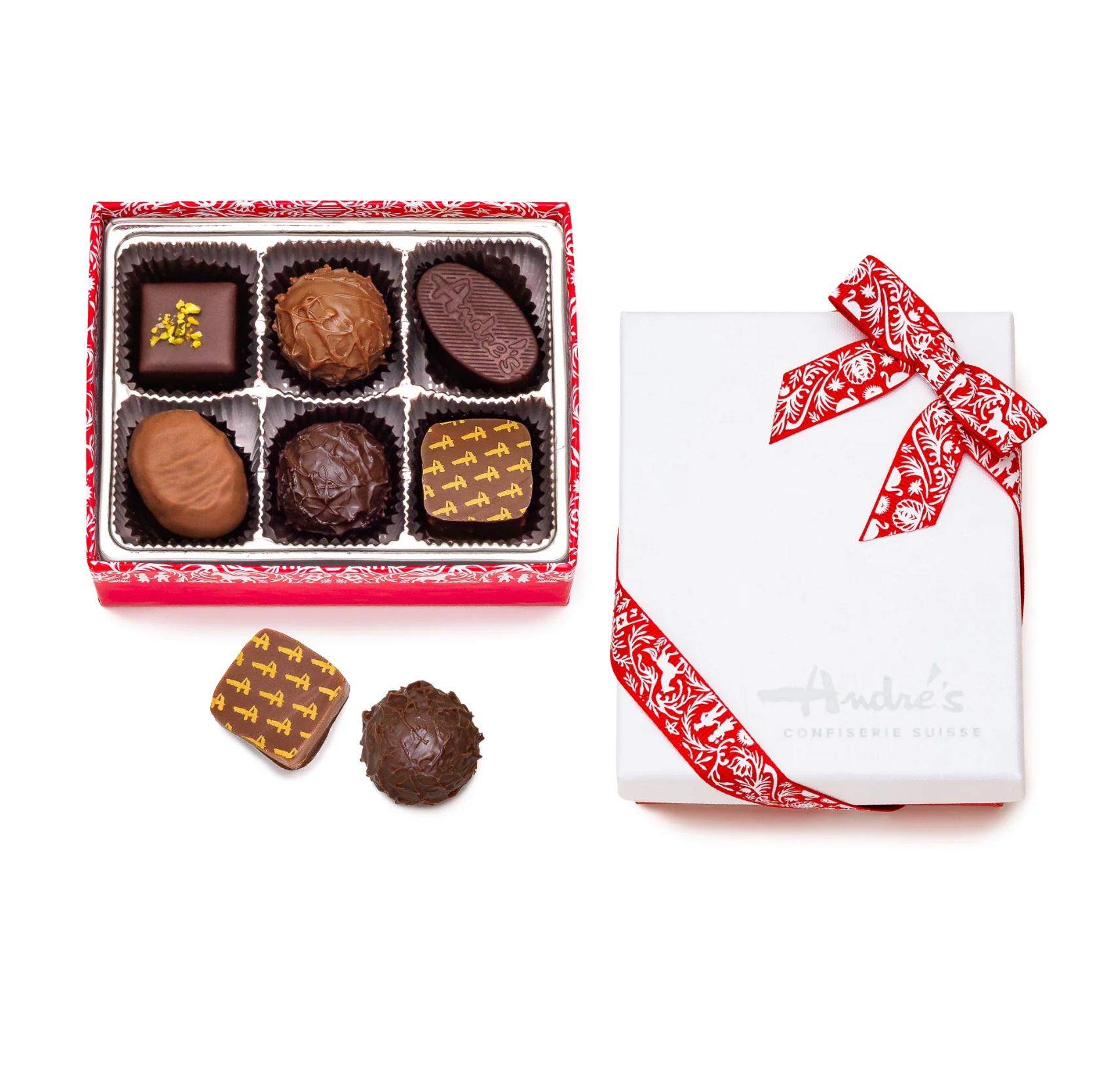 An assortment of gourmet chocolates displayed in a red gift box next to its white lid with a red paisley ribbon, with two chocolates placed outside the box on a white background. The brand 'Andre's Confiserie Suisse' is visible on the lid.