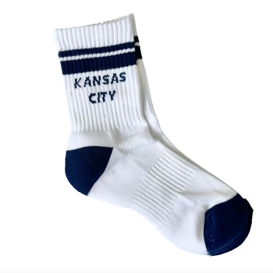 A single white crew sock with navy blue stripes and 'KANSAS CITY' embroidered on the cuff, shown on a plain white background.