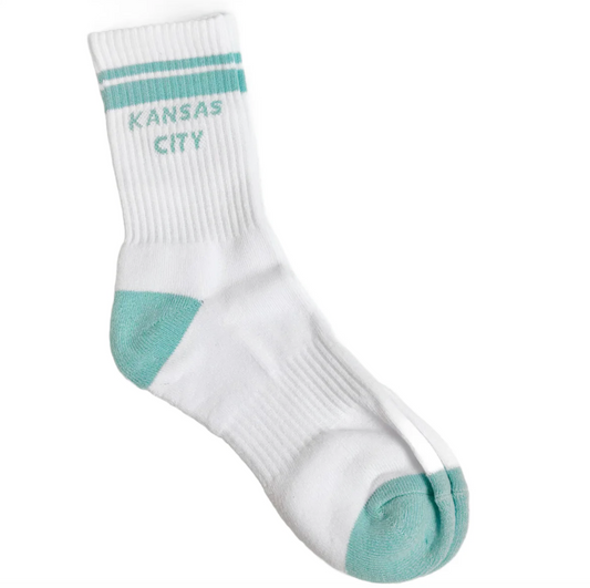 A single white crew sock with mint green accents, featuring 'KANSAS CITY' printed in mint green on the ribbed ankle area with two horizontal mint green stripes above it. The sock is photographed on a clean white background.