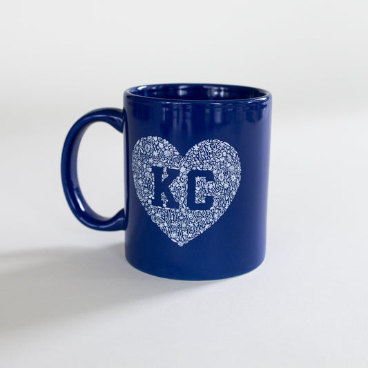 A dark blue ceramic mug with a white heart-shaped monogram design featuring the letters 'KC' in the center, set against a plain light gray background.