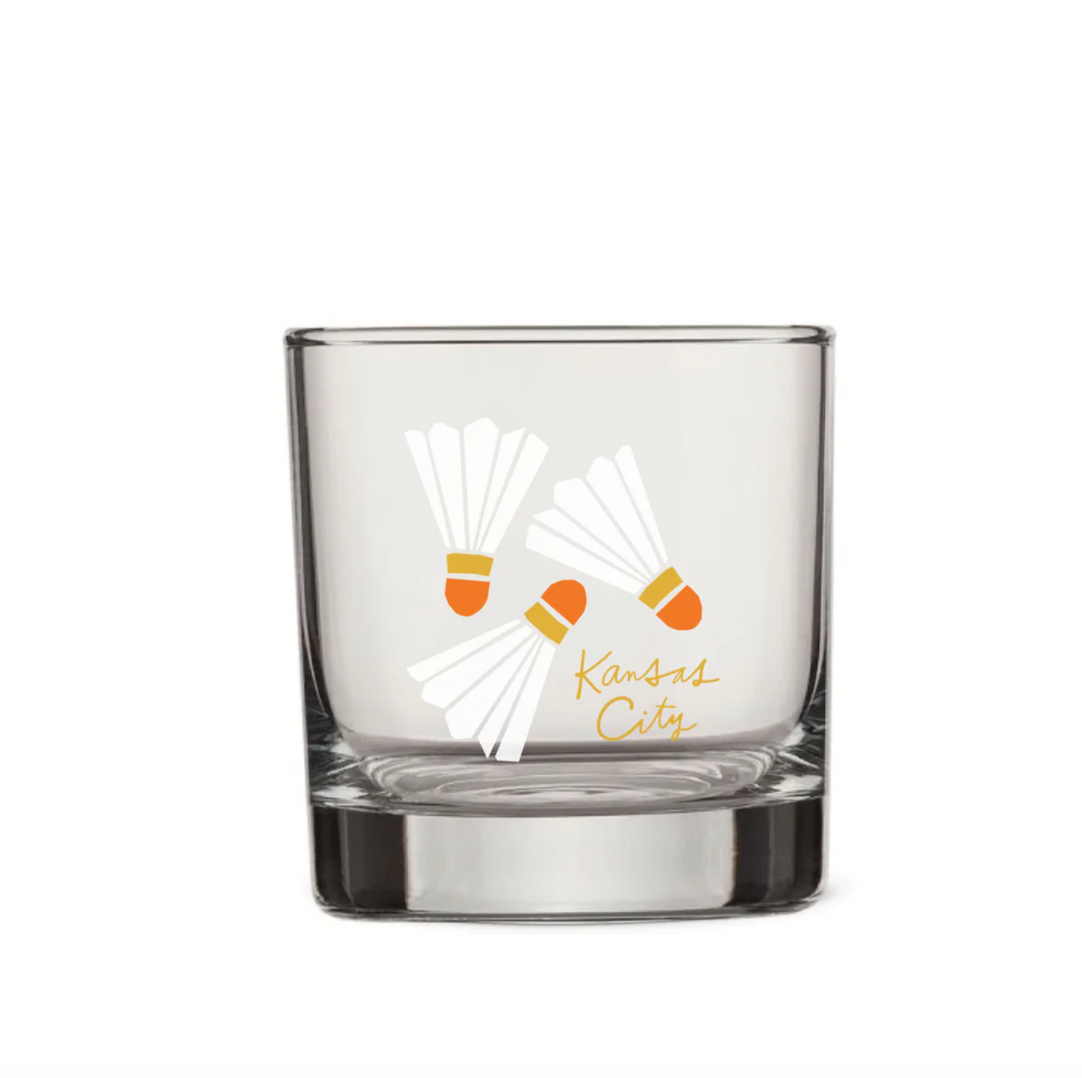 A clear glass rocks tumbler featuring a white shuttlecock graphic with orange accents and the gold script text 'Kansas City' on the front, set against a plain white background.