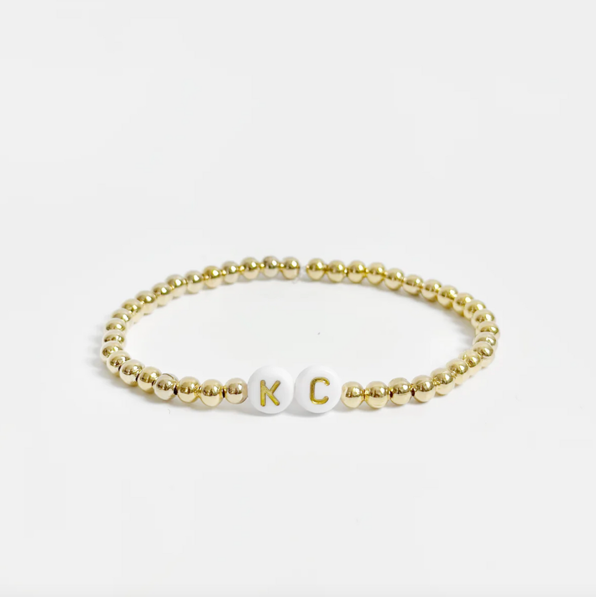 Gold beaded friendship bracelet with white and gold letter beads spelling out "KC" 