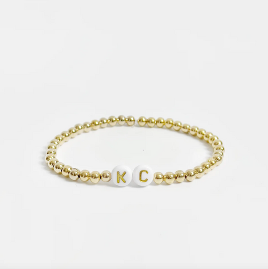 Gold beaded friendship bracelet with white and gold letter beads spelling out "KC" 