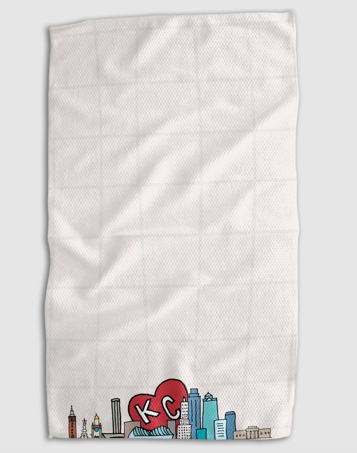 A white textured kitchen towel with a grid pattern, featuring a colorful Kansas City skyline graphic and a red heart with 'KC' in white at the bottom, shown against a light gray background.