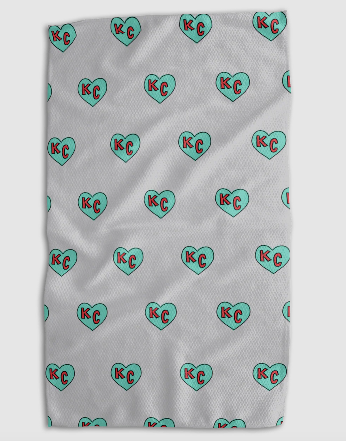 A white textured blanket featuring a repeating pattern of mint green hearts with red 'KC' initials inside, shown flat against a light gray background.