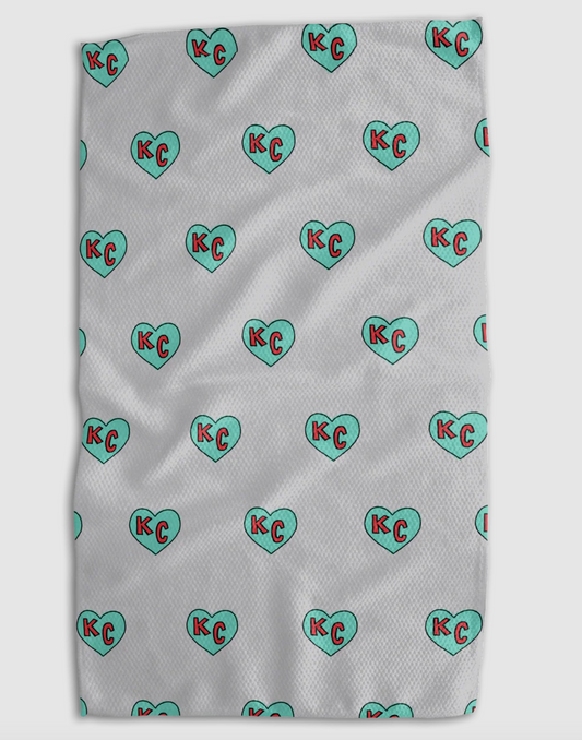 A white textured blanket featuring a repeating pattern of mint green hearts with red 'KC' initials inside, shown flat against a light gray background.