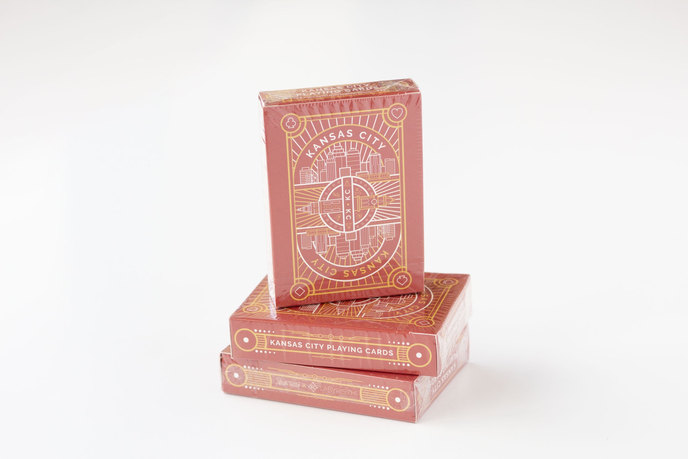 Three decks of Kansas City playing cards stacked on a white background, featuring a reddish-brown card back with gold line art and text.