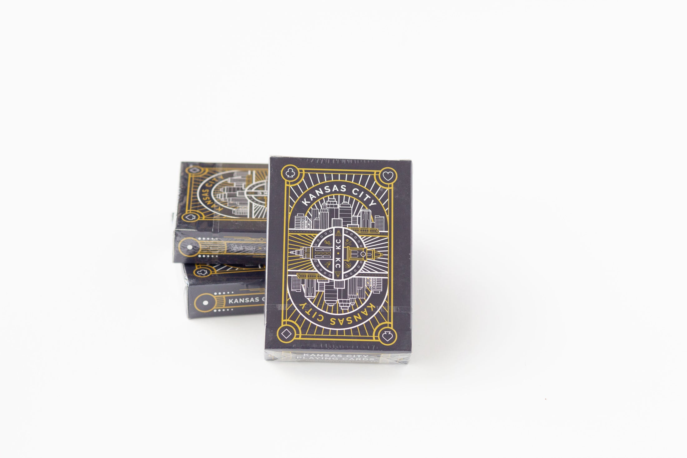 A deck of playing cards with a dark gray and gold map design, standing upright next to two stacked decks on a white background.