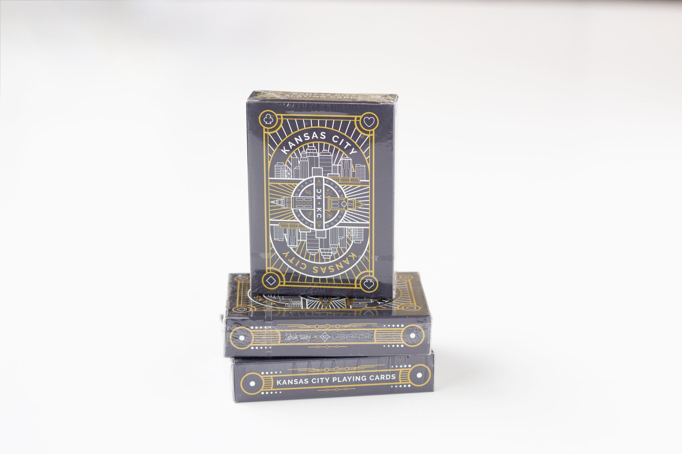 A stack of Kansas City Playing Cards in a black box with gold and white geometric designs, photographed on a clean white background.