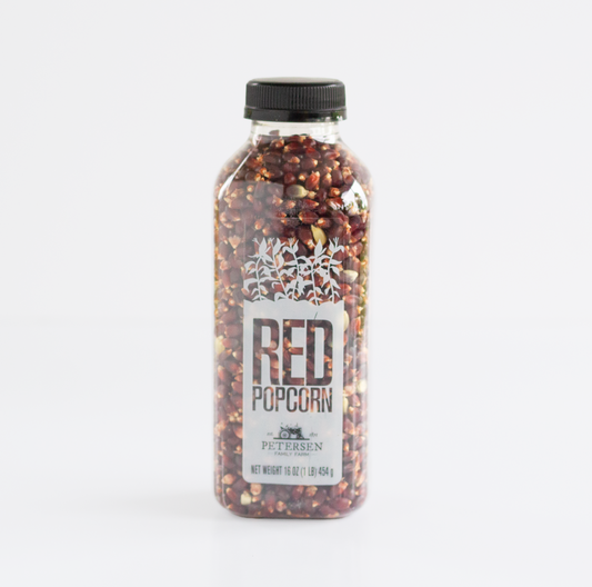 A clear plastic bottle filled with red popcorn kernels, sealed with a black cap, and labeled 'RED POPCORN' with 'Petersen' visible on the front, photographed on a clean white background.