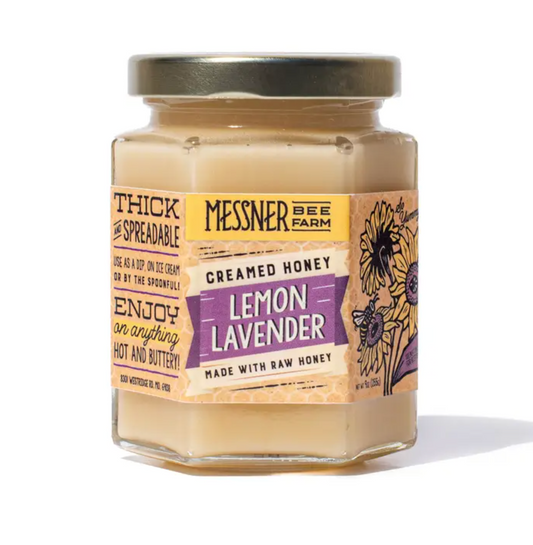 a jar of Lemon Lavender Creamed Honey from Messner Bee Farm, made with raw honey. The packaging is yellow and purple to reflect the flavor variety. 