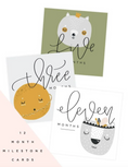 Load image into Gallery viewer, Three baby milestone cards shown on a white background with a pale pink corner accent. The cards feature illustrated animals and handwritten text reading 'five months,' 'three months,' and 'eleven months,' with additional text at lower left reading '12 MONTH MILESTONE CARDS.
