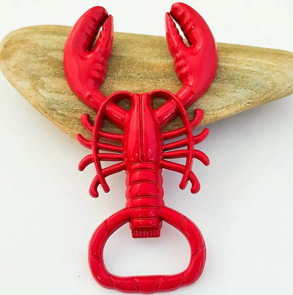 A bright red lobster-shaped bottle opener displayed on a light tan stone against a white background.