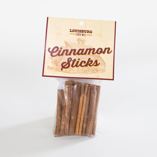 A clear plastic bag containing several cinnamon sticks, attached to a cream-colored paper header card with the text 'Louisburg Cider Mill Cinnamon Sticks' and a sepia illustration of the Louisburg Cider Mill.