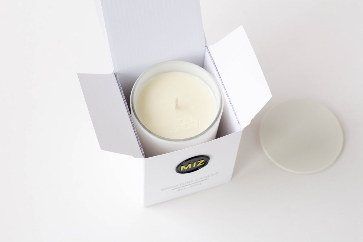An open white candle box containing a white wax candle, with the brand logo 'MIZ' visible on the front. A matching white lid sits to the right on a clean white background.