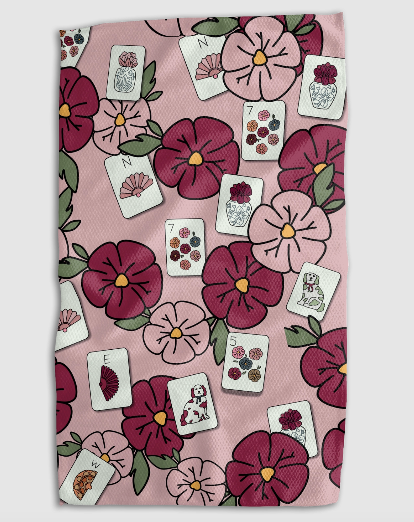 A square textile item, likely a tea towel or hand towel, featuring a pink background with a repeating pattern of dark pink and burgundy flowers, green leaves, and white playing cards.