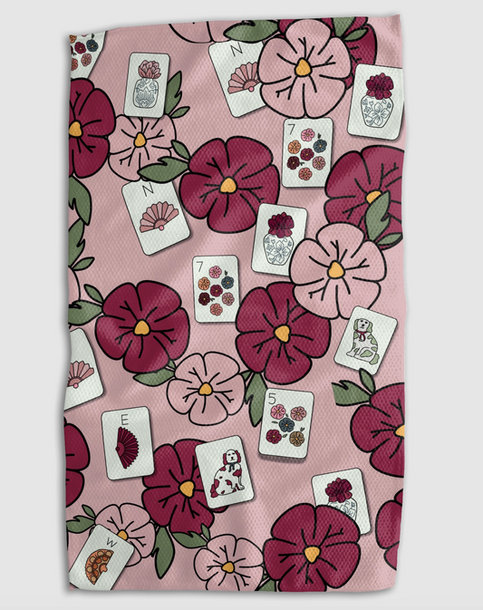 A square textile item, likely a tea towel or hand towel, featuring a pink background with a repeating pattern of dark pink and burgundy flowers, green leaves, and white playing cards.