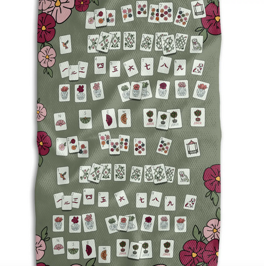 A flat-lay view of a rectangular game board or mat with a sage green background, decorated with pink and magenta floral corners and rows of small illustrated playing cards.