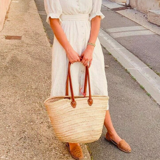 a woman in a long white dress holds a woven market tote with long leather straps