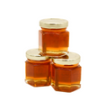 Load image into Gallery viewer, Three small hexagonal glass jars filled with amber honey, arranged in a pyramid stack with shiny gold metal lids on a plain white background.
