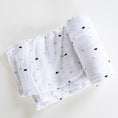 Load image into Gallery viewer, A white muslin baby swaddle blanket with a small black and gray heart pattern, folded and rolled on a light off-white background.
