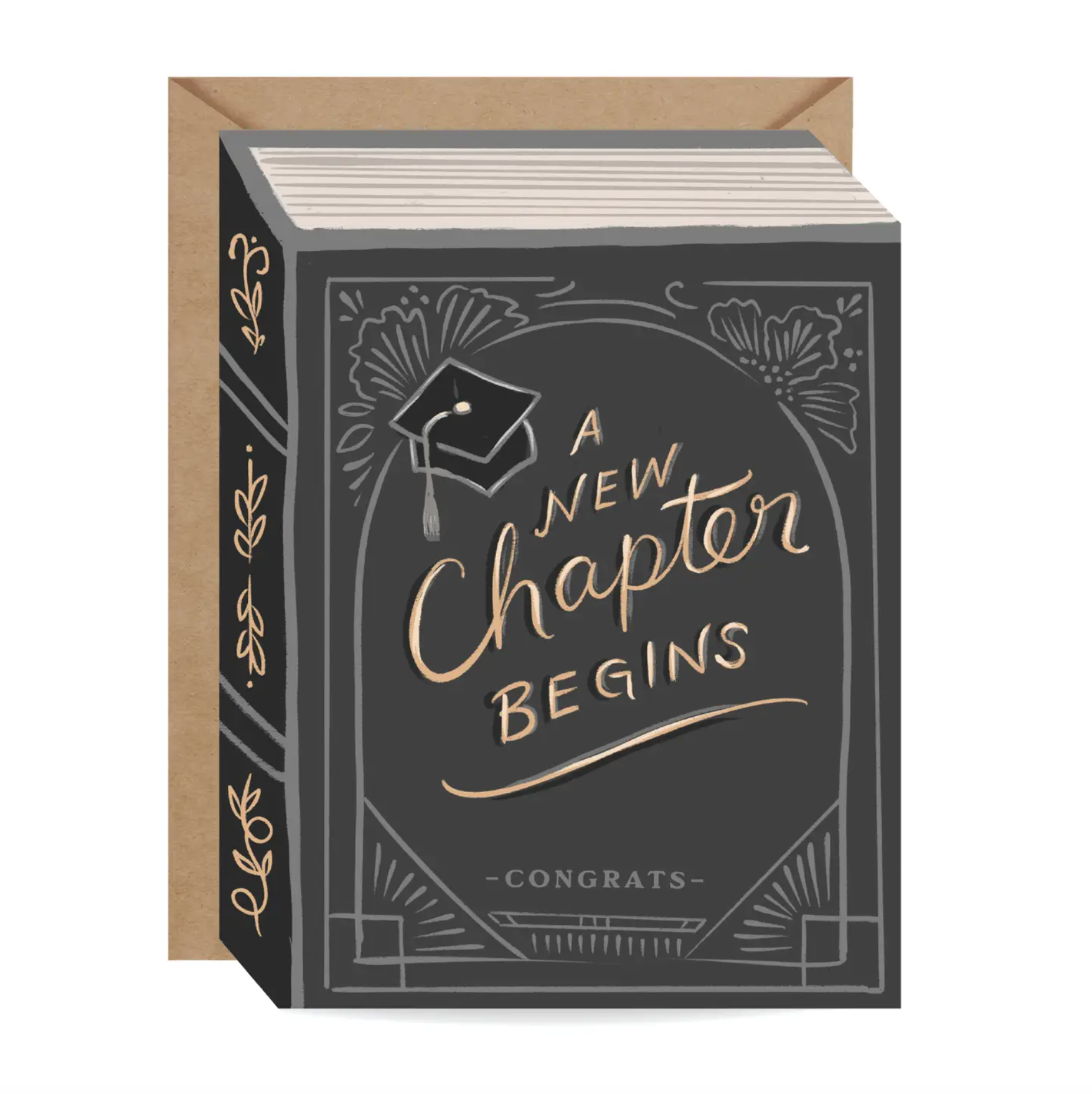 A graduation-themed greeting card designed to look like a hardcover book, with a kraft paper envelope behind it. The dark gray book cover features gold foil-style lettering that reads 'A New Chapter Begins' and 'Congrats', along with a graduation cap illustration and decorative borders.