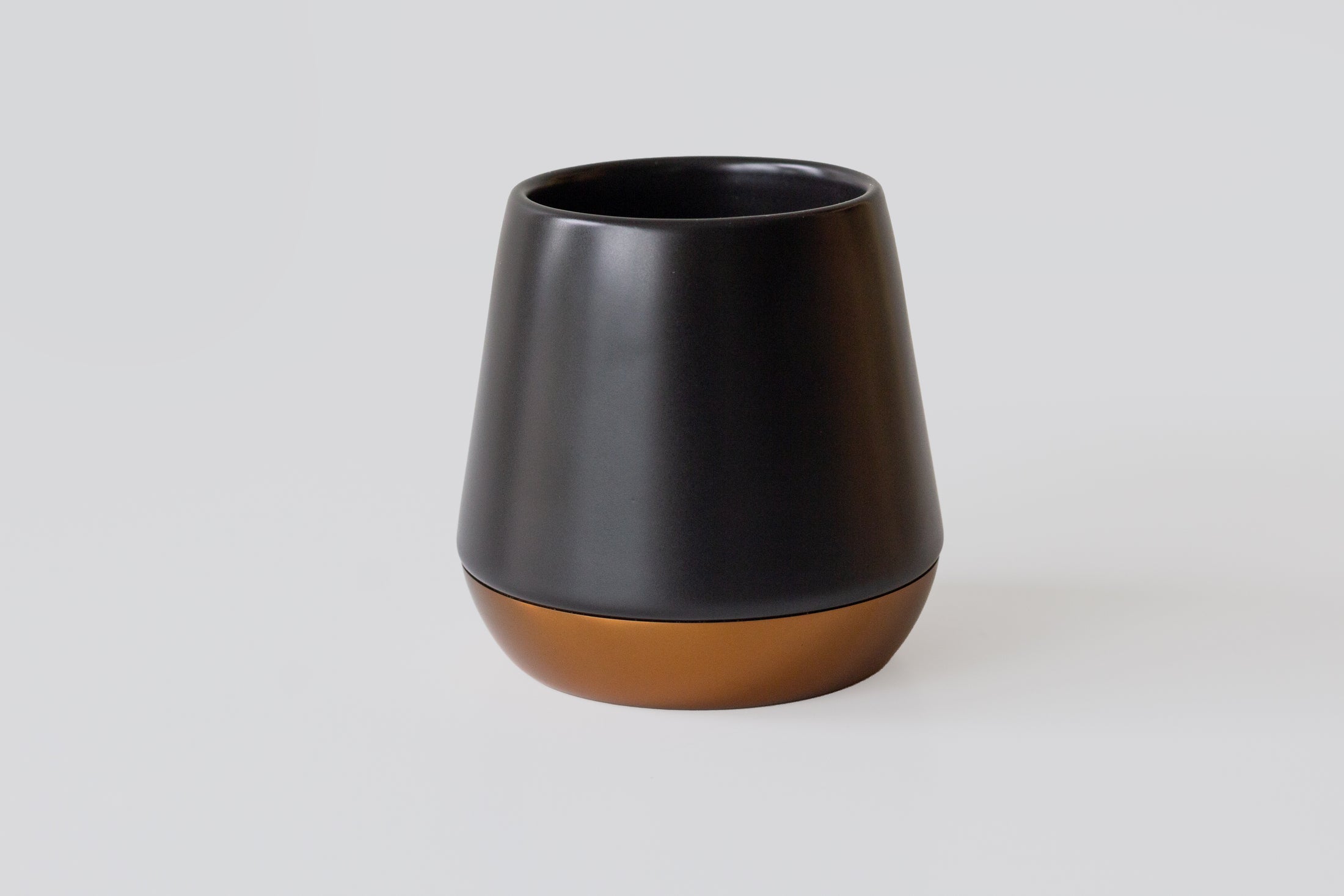 A modern tapered insulated Joey Mug with a matte black upper body and a metallic bronze base, photographed on a clean light gray background.