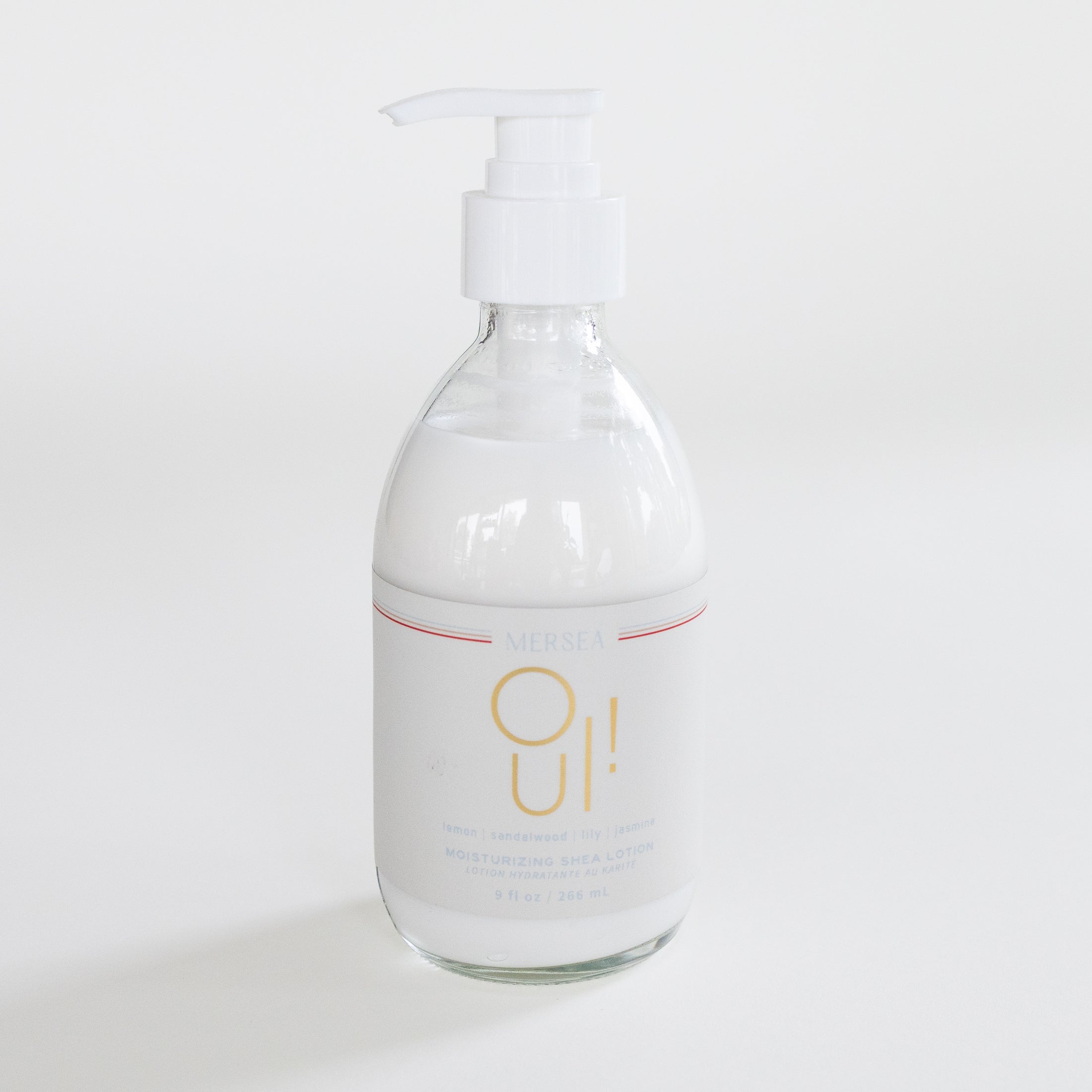 Mersea Oui! Moisturizing Shea Cream in a clear glass bottle with a white pump dispenser and a white label featuring gold lettering, set against a clean white background.