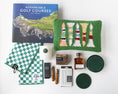 Load image into Gallery viewer, A curated flat lay of golf-themed merchandise on a white background, including a book titled 'Remarkable Golf Courses' by Iain Spragg, a green textured pillow with multi-colored golf tees, a green checkered towels, a white candle with a green plaid wax seal, bourbon-soaked toothpicks in both glass jars and cardboard packaging, a shoe shine kit in a wood grain box, silver plated cocktail picks, a bottle of black walnut cocktail bitters, and a set of green leather coasters. 
