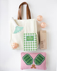 Load image into Gallery viewer, A coordinated pickleball gift set on a white background, including a cream canvas tote bag with brown handles, a green and white checkered pickleball book, a mint-and-white striped pickleball paddle, a pink woven pickleball pillow with green net embroidery, three peach-orange pickleballs, and a brown box labeled LUXE.
