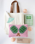 Load image into Gallery viewer, A coordinated pickleball gift set on a white background, including a cream canvas tote bag with brown handles, a green and white checkered pickleball book, a mint-and-white striped pickleball paddle, a pink woven pickleball pillow with green net embroidery, three peach-orange pickleballs, and a brown box labeled LUXE.
