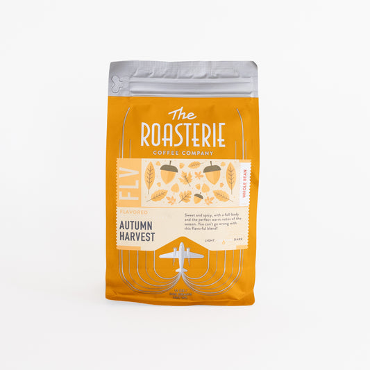 A stand-up coffee bag of The Roasterie Coffee Company's 'Autumn Harvest' whole bean coffee, featuring a bright orange-yellow design with a silver resealable top, set against a plain white background.