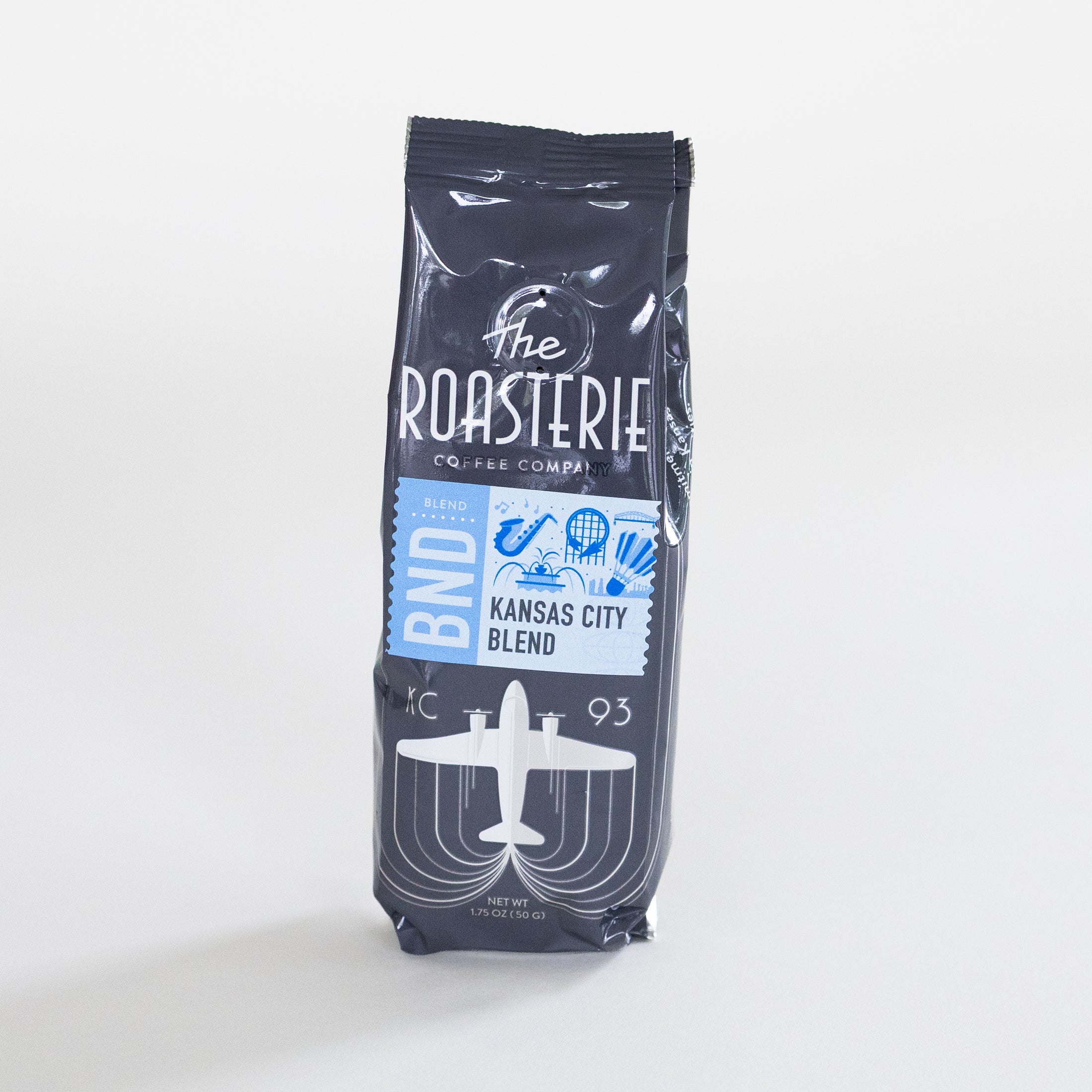 A 1.75oz bag of The Roasterie Coffee Company Kansas City Blend coffee, featuring a dark navy blue package with white and light blue graphics, set against a plain light gray background.