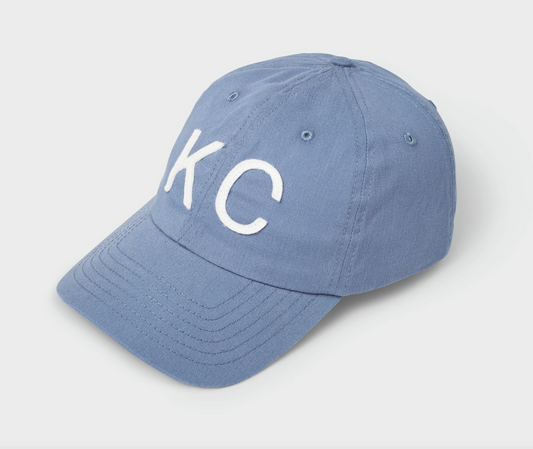 A light blue cotton baseball cap with white embroidered letters 'KC' on the front, photographed on a clean light gray background.