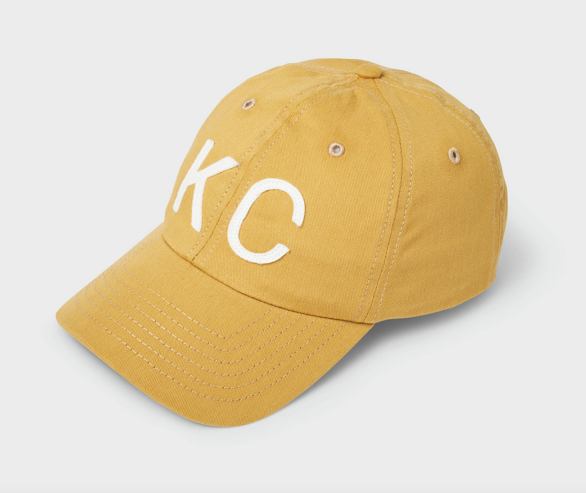 A yellow cotton baseball cap with white embroidered letters 'KC' on the front, photographed on a light gray background.