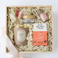 Load image into Gallery viewer, A curated gift box set on a white background, containing a beige candle, a small pink bottle of matches, a Big Heart Tea Cup of Love tea box, and a jar of Someday Sunday Body Lotion, all nestled in white paper krinkle inside a light wood box with a pale pink ribbon.
