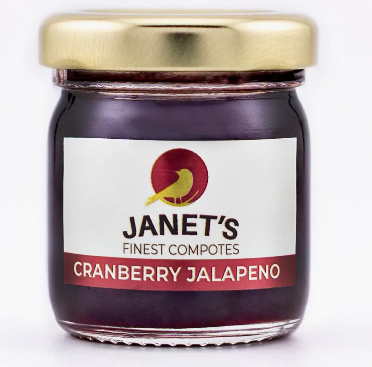 A glass jar of Janet's Finest Compotes Cranberry Jalapeño jam with a gold metal lid and a white label, shown against a plain white background.
