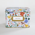 Load image into Gallery viewer, A rectangular metal recipe box with a lid, decorated with a colorful floral and botanical print on a white background. It features a gold-colored trim and a white label with a gold border that reads 'RECIPES'.
