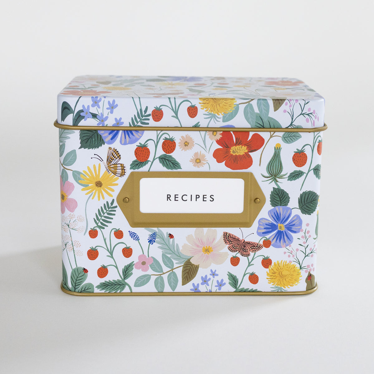 A rectangular metal recipe box with a lid, decorated with a colorful floral and botanical print on a white background. It features a gold-colored trim and a white label with a gold border that reads 'RECIPES'.