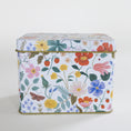 Load image into Gallery viewer, A square metal tin with a colorful floral and botanical print on a white background, featuring pink, red, yellow, blue, and green flowers with leaves, berries, and a butterfly. The tin has a gold-toned metal rim and is photographed against a clean, light off-white background.
