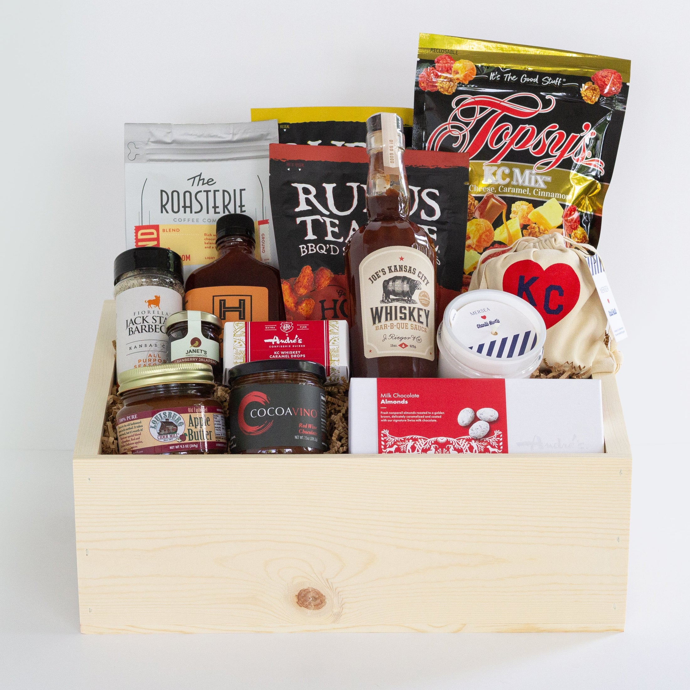 A wooden gift box filled with assorted gourmet Kansas City snacks, tea, coffee, and packaged food items, photographed against a clean white background.