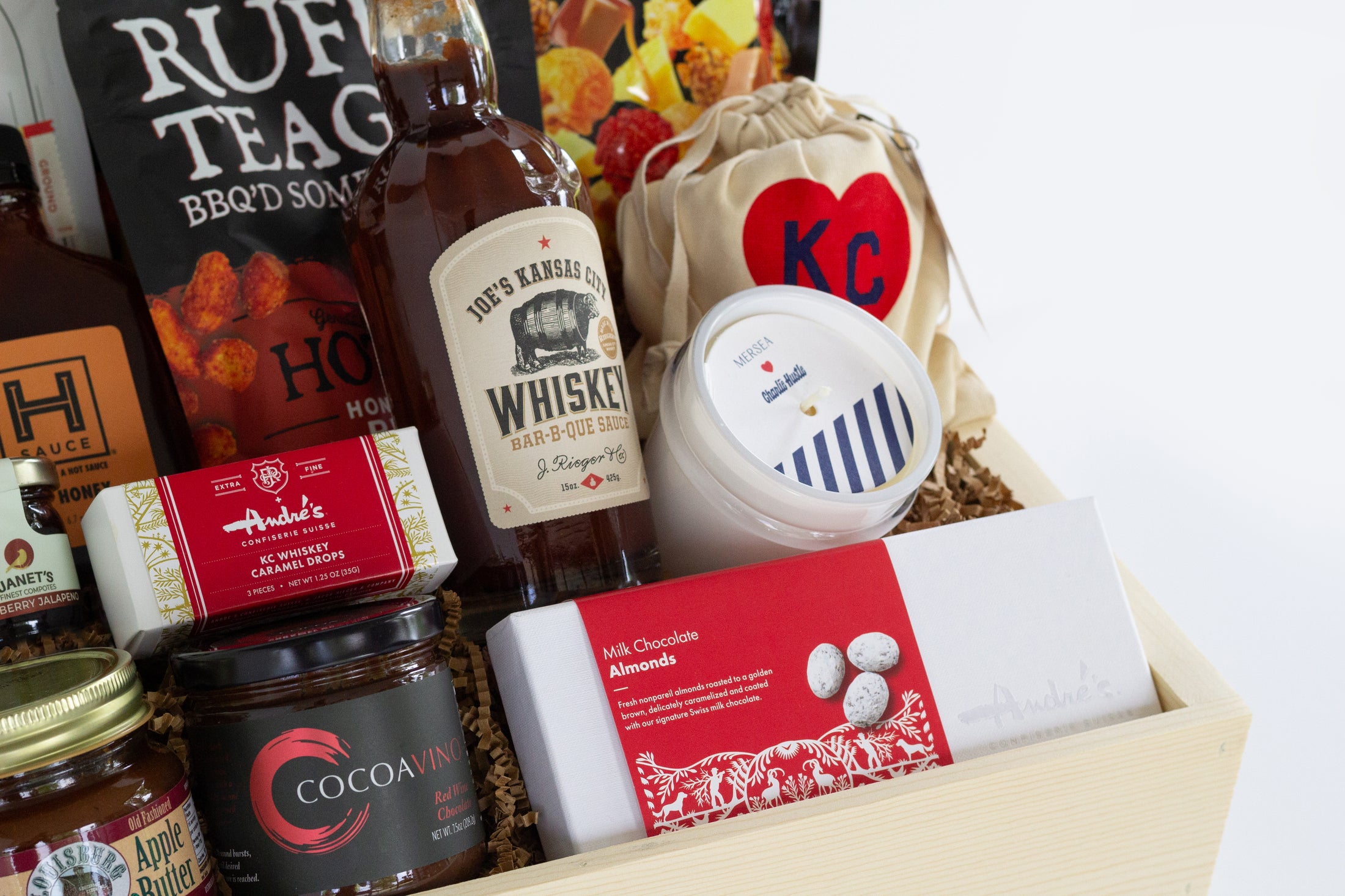 A wooden gift box filled with assorted gourmet Kansas City snacks, tea, coffee, and packaged food items, photographed against a clean white background.