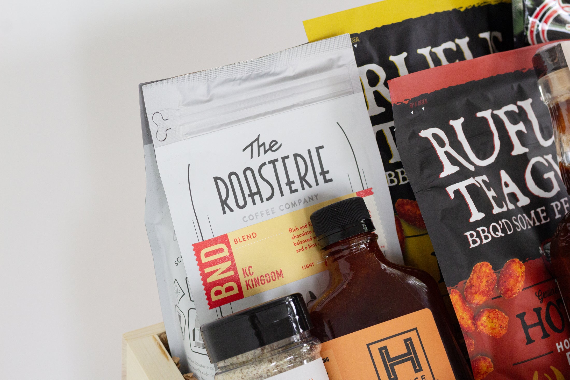 A wooden gift box filled with assorted gourmet Kansas City snacks, tea, coffee, and packaged food items, photographed against a clean white background.