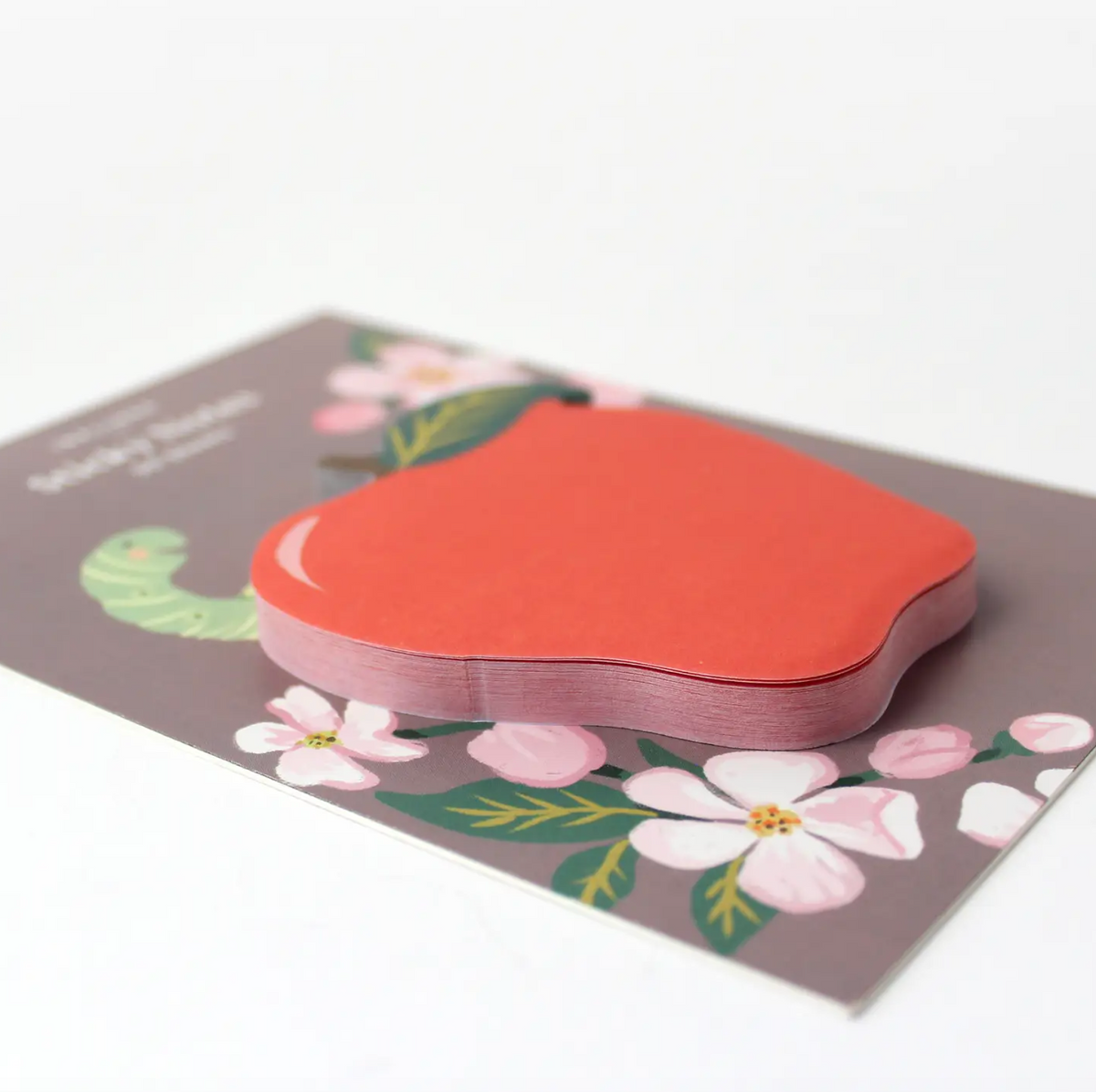 Apple-shaped sticky notes on a brown backing card that features florals and a green worm sticking out of the worm.