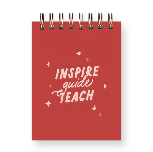 A small spiral-bound notepad in red with the words "Inspire, Guide, Teach" on the cover