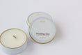 Load image into Gallery viewer, Two round tin candles on a clean white background, including one open candle showing the wax and wood wick, and one closed lids with the label 'Wedding Day' and brand 'effing candle co'.
